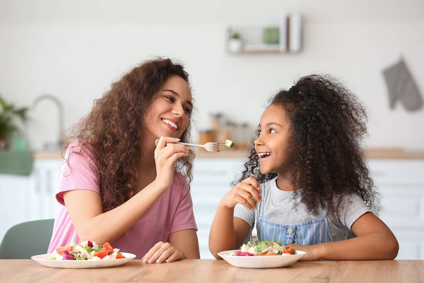 Afro-Amerikaans klein meisje met haar moeder eten verse salade in de keuken - Foto, afbeelding