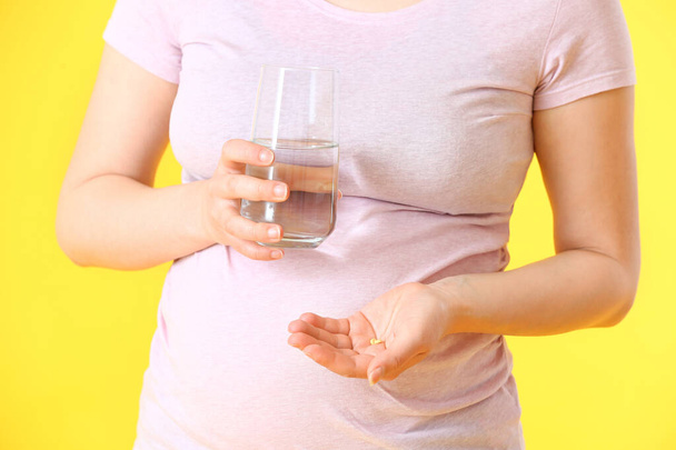 Mladá těhotná žena s pilulky a sklenice vody na barevném pozadí - Fotografie, Obrázek