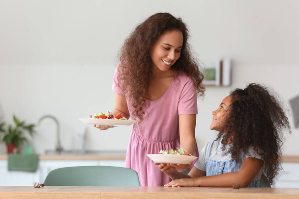 Menina afro-americana com sua mãe comendo salada fresca na cozinha - Foto, Imagem