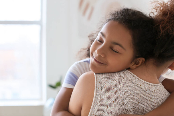 Afro-Amerikaans meisje knuffelen haar moeder thuis - Foto, afbeelding