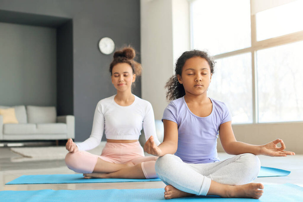African-American little girl with her mother practicing yoga at home - Foto, imagen