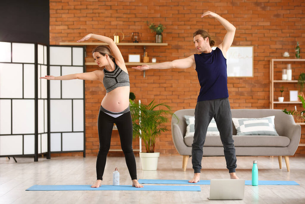 Giovane donna incinta e suo marito praticare yoga a casa - Foto, immagini