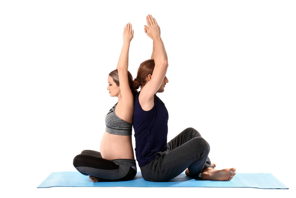 Fiatal terhes nő és férje gyakorló jóga fehér háttér - Fotó, kép