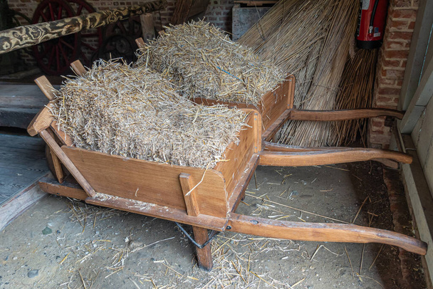 Genk, Bélgica - 11 de agosto de 2021: Domein Bokrijk. Un par de carretillas de madera beige cargadas con paja seca de pie en el granero. - Foto, Imagen