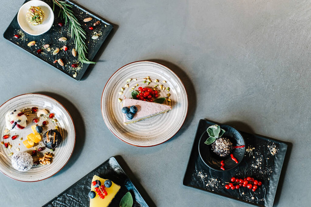 Top View of Table full with Different Protein Balls and Healthy Cakes.Directly above photo of sugar free desserts with fruits and nuts: few healthy energy balls and fruit cakes served on black plates in a restaurant table with copy space. - 写真・画像