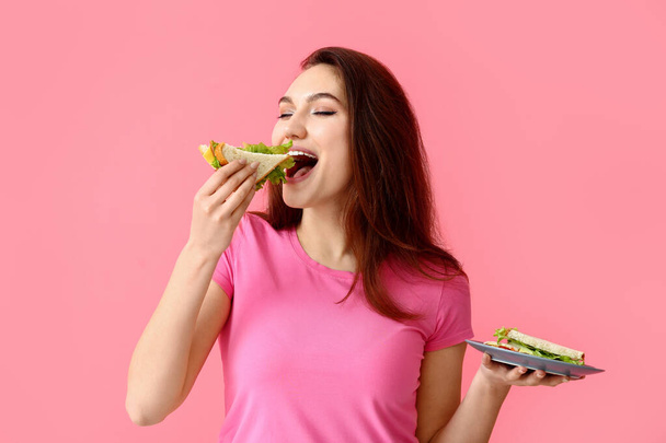 Young woman eating tasty sandwich on color background - Photo, Image