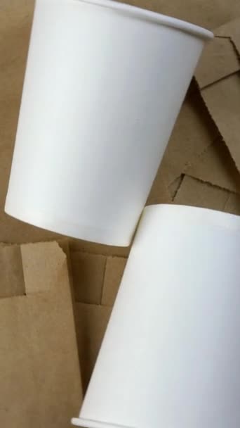 Lege papieren verpakking, milieuvriendelijke wegwerpbare biologisch afbreekbare verpakking voor goederen en lege papieren beker. Draait in cirkel. Milieuvriendelijke achtergrond. Verticale video. Bovenaanzicht. - Video