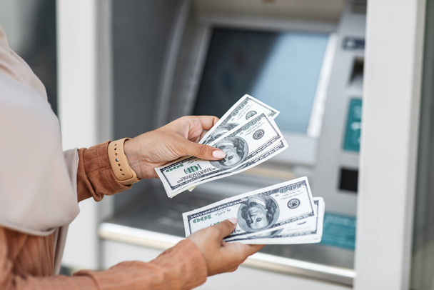 Nierozpoznawalne millenium arabski lady liczy wiele dolarów w pobliżu ATM outdoor - Zdjęcie, obraz