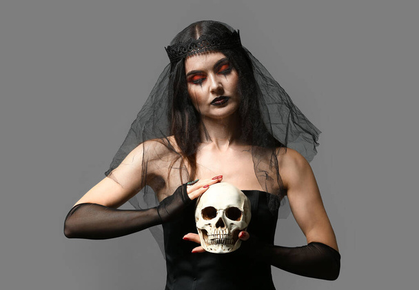 Jeune sorcière avec crâne sur fond gris - Photo, image