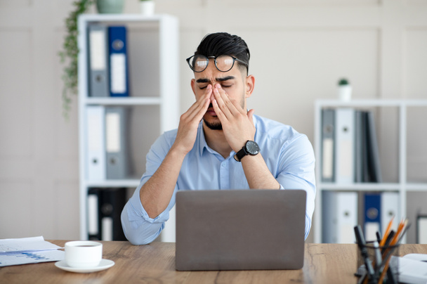 Millennial empleado árabe frotando cansados ojos irritados, trabajando con el ordenador portátil demasiado, agotado de trabajo en línea en la oficina - Foto, imagen