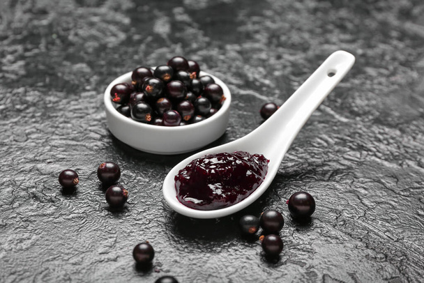 Bowl with berries and delicious black currant jam in spoon on dark background - Foto, Bild