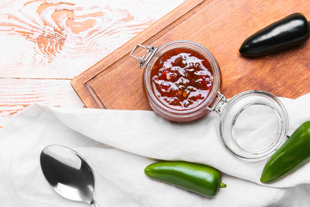 Jar with delicious jam and jalapeno peppers on light wooden background - 写真・画像