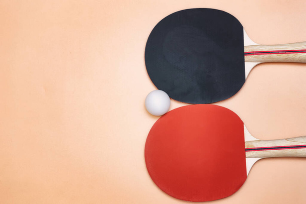 Des raquettes de ping-pong rouges et noires et une balle de ping-pong reposent sur un fond beige. Il y a une place pour le texte - Photo, image