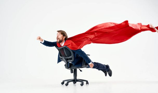 бизнесмен в красном плаще примеряет на себя офисное кресло супермена - Фото, изображение