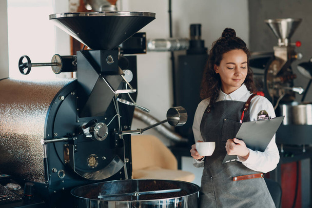 Café tostadora y barista mujer con la tableta escribir pluma en el proceso de tostado de café - Foto, imagen