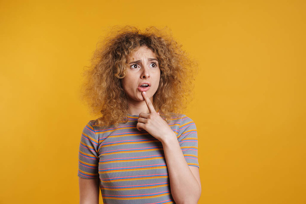 Confused young blonde woman in casual clothes standing over yellow background - 写真・画像