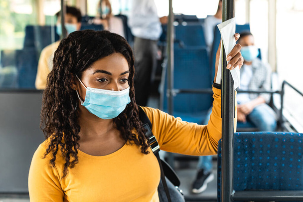 Чорна жінка в хірургічній масці стоїть в автобусі з використанням тканини
 - Фото, зображення