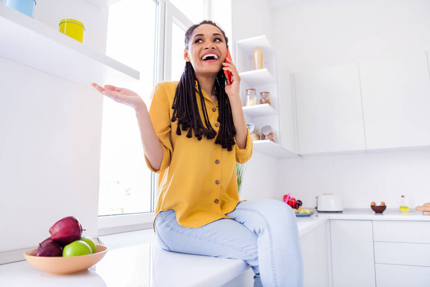 Photo of charming excited dark skin lady wear yellow shirt sitting table talking modern gadget indoors room home house - Φωτογραφία, εικόνα