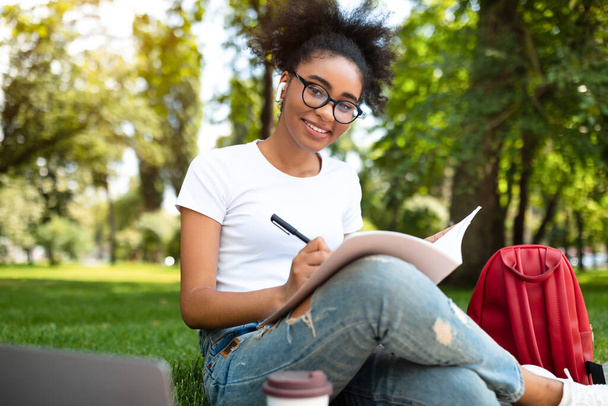 allegro nero college ragazza prendere appunti apprendimento seduta in parco - Foto, immagini