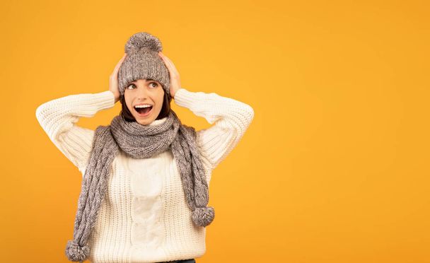 Its unbelievable. Surprised young lady in warm sweater and knitted set being shocked to see sales, yellow background - Foto, Imagem