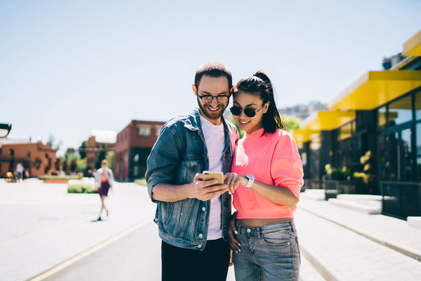 Millennial friends checking online information about together web blog smiling during mobile networking, happy male and female Generation Z in trendy glasses watching media video via cellphone app - Photo, image