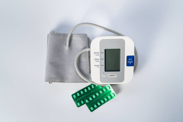 Monitor de presión arterial para tomar presión arterial y pastillas para bajarla sobre fondo blanco. - Foto, imagen