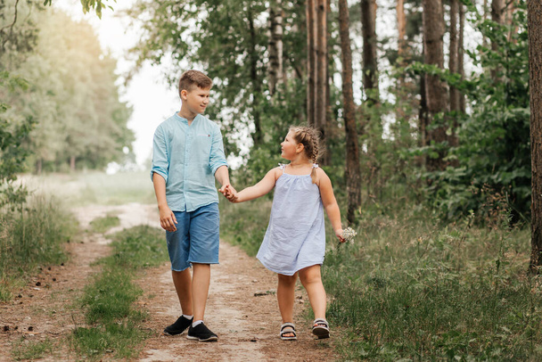 Ένα αγόρι και ένα κορίτσι, αδελφός και αδελφή περπατούν μαζί σε ένα δασικό μονοπάτι. - Φωτογραφία, εικόνα