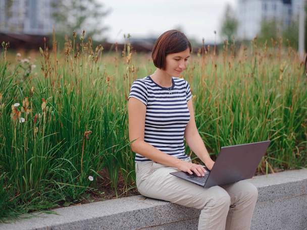Modern üniversite kampüs parkında dizüstü bilgisayarla çalışan bir kadın.. - Fotoğraf, Görsel