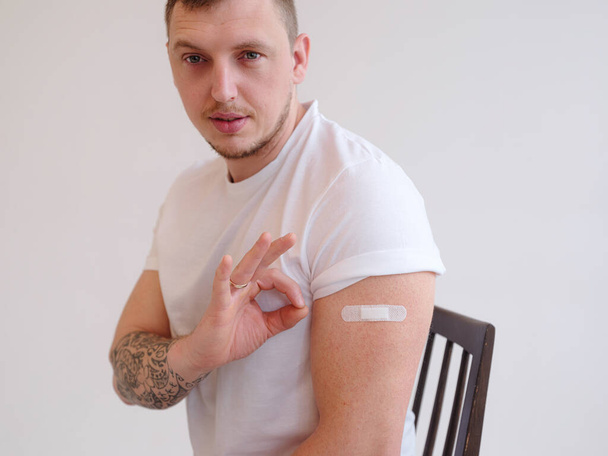 Улыбающийся взрослый кавказский мужчина показывает плечо с пластырем после инъекции - Фото, изображение