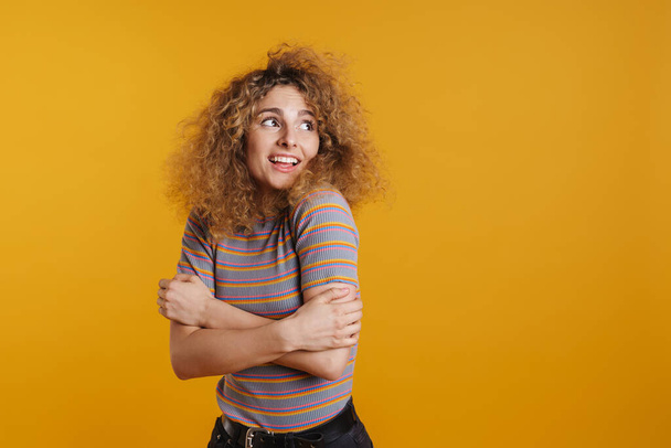 Boldog mosolygós fiatal szőke nő fizzy haj alkalmi ruhák áll a sárga fal felett háttér, félrenéz - Fotó, kép