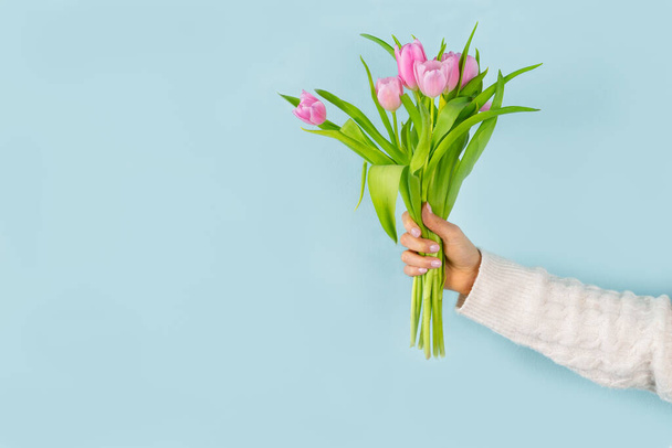 Mano di donna che tiene un mazzo di tulipani rosa su sfondo blu. Idea primaverile. Copia spazio a sinistra. - Foto, immagini