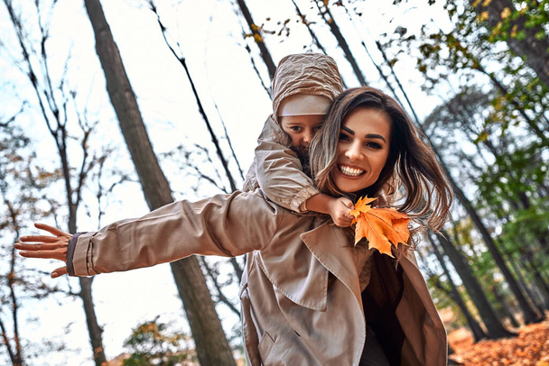 Cheerful emotions. Mom and daughter having fun in the autumn park. Mom holds daughter on shoulders playing pilot, superhero. - Foto, afbeelding