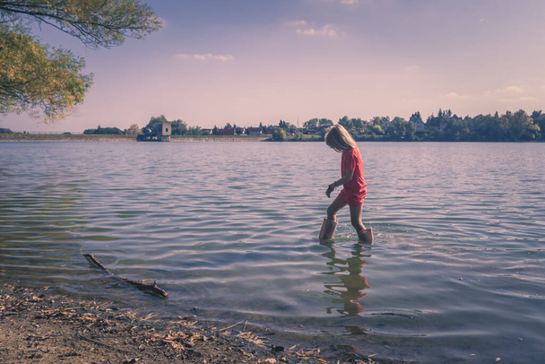 ウェリントンブーツを着た可愛い女の子が川に立っていて - 写真・画像