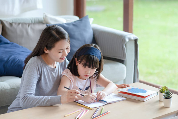 Asian mother teaching her cute kid daughter to studying in living room at home - Photo, Image