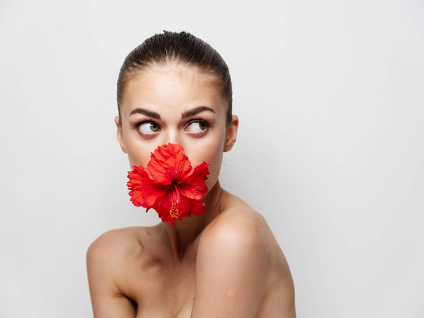 привлекательная женщина с голыми плечами и красным цветком во рту обрезанный вид - Фото, изображение