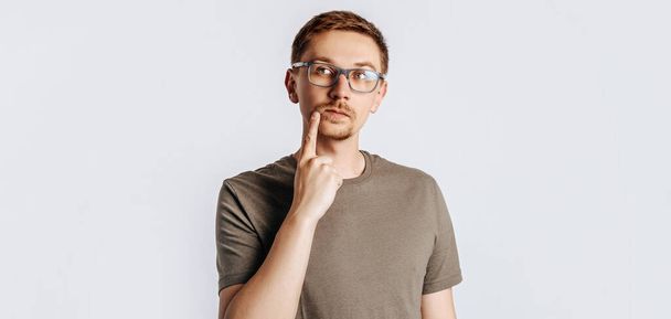 Young handsome man with glasses a brunette beard. Student, worker, businessman posing for photo isolated on gray background. Place for advertising. - Fotó, kép