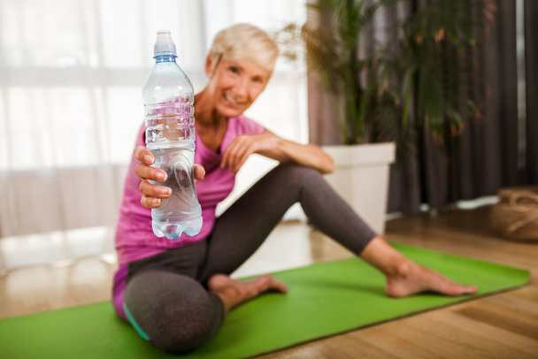 熟女の運動や柔軟性の演習を行う彼女の体を伸ばす、彼女は運動後に水を飲む. - 写真・画像