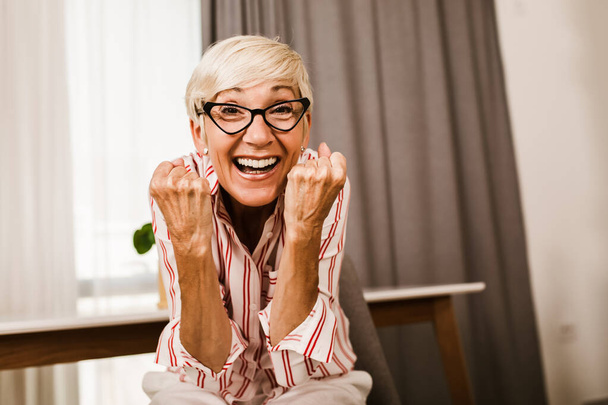 Portret szczęśliwej seniorki gestykulującej rękami w domu. - Zdjęcie, obraz