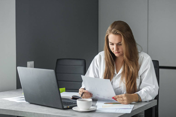 Strict woman at work. Business smart woman working in the office. Convenient workplace. Distant work. Earn extra money. Modern office. A white blouse. - Photo, Image