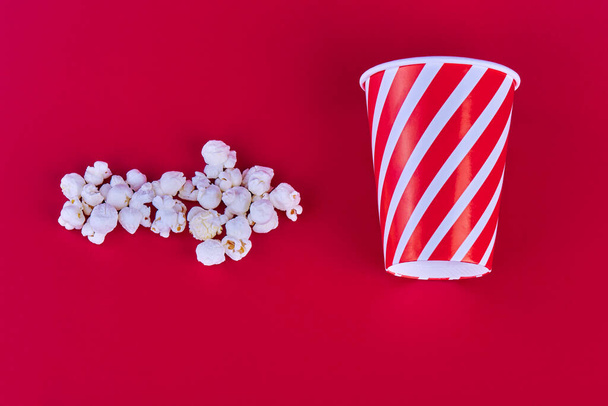 A white popcorn arrow points to the glass to the right. The glass stands flat, on a red background. - Φωτογραφία, εικόνα