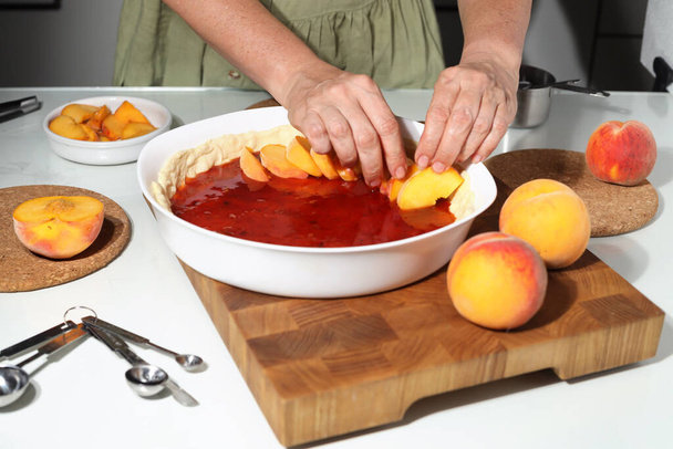 Домогосподарка готує свіжий персиковий пиріг. Процес домашнього випікання. Жінка поклала свіжий персик на тортну скоринку
 - Фото, зображення