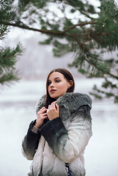 Muoti lähikuva muotokuva melko luottavainen nainen seisoo poseeraa ulkopuolella katupuisto luonto pukeutunut trendikäs ympäristöystävällinen keinotekoinen turkis takki talvivaatteita nenä lävistyksiä kasvot isot huulet - Valokuva, kuva
