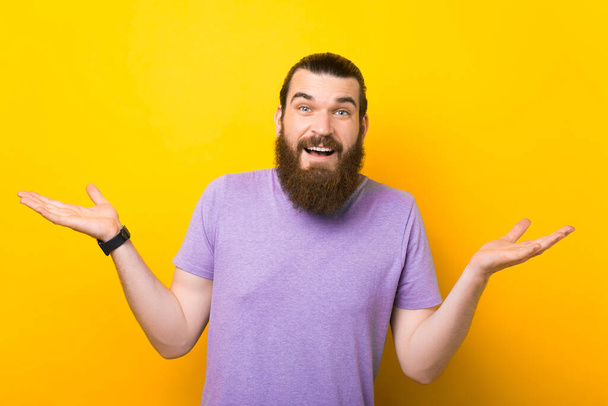 Photo of a confused bearded man is shrugging over yellow background. - Φωτογραφία, εικόνα