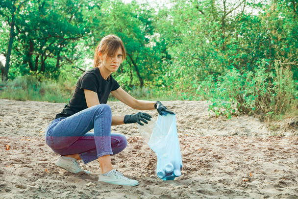 Young woman volunteer collects trash in trash bag rubbish in nature. Environment and plastic waste. - Photo, image