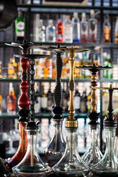 Multicolored beautiful hookahs stand on the table on the background of alcohol at the bar. Trendy hookah. active recreation concept with hookah. - Foto, Imagen