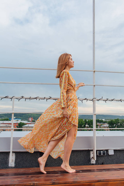 Kaunis nuori nainen pitkä leopardi mekko seisoo paljain jaloin portaissa katolla rakennuksen. - Valokuva, kuva
