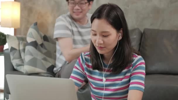 Aasian nainen käyttää kannettavaa tietokonetta online-liiketoimintaa, verkkokaupan chat, ja internet-oppiminen, hänen veljensä sohvalla takana. Molemmat sisarukset työskentelevät kotona, koska he joutuvat karanteeniin COVID-19. - Materiaali, video