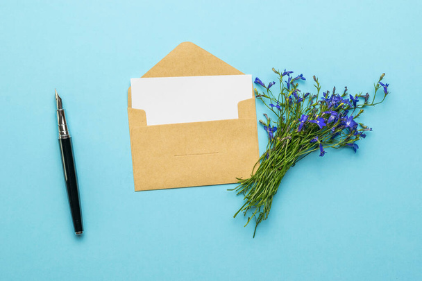 Een envelop met een brief, een vulpen en een boeket bloemen op een blauwe achtergrond. Het concept van liefdescorrespondentie. Vlakke plaat. - Foto, afbeelding