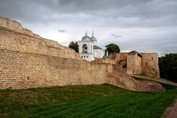 View of the wall of the Izborsk fortress, the Nikolsky Gate and St. Nicholas (Nikolsky) Cathedral (XIV-XVII century) on a cloudy summer day. Stary Izborsk, Pskov region, Russia - Photo, Image