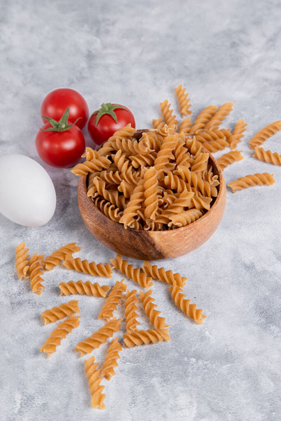 Een houten kom Italiaanse ongekookte droge pasta Fusilli rigeren met tomaten. Hoge kwaliteit foto - Foto, afbeelding